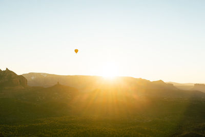 Wide shot of single hot air balloon in sky as sun rises above red rock mountains in sedona arizona.