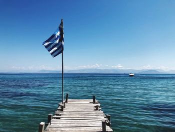 Flag on pier over sea against blue sky