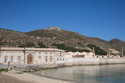 Calm sea in front of houses against clear blue sky