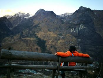 Woman sitting on mountain against sky