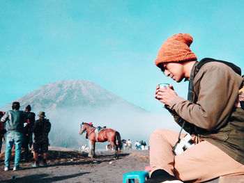 Man drinking while sitting against sky