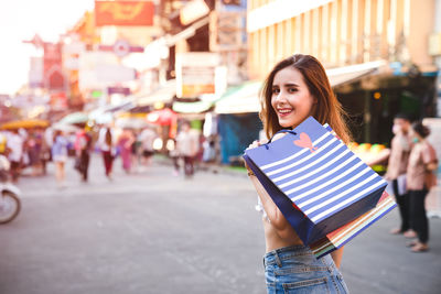 Portrait of smiling young woman holding umbrella on street in city