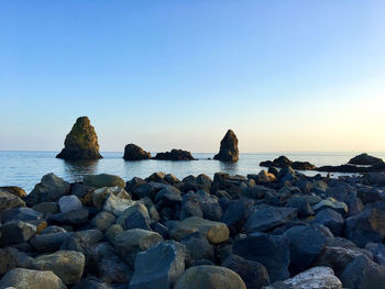 Rocks on sea shore against clear blue sky