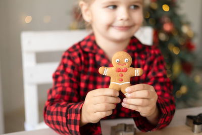 Little girl in red pajama cooking festive gingerbread in christmas decorated kitchen