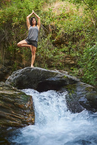 Young woman practicing yoga in a river. she's in the middle of nature.