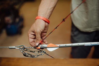 Unrecognizable male with modern bow and arrows standing in garage and preparing for hunting