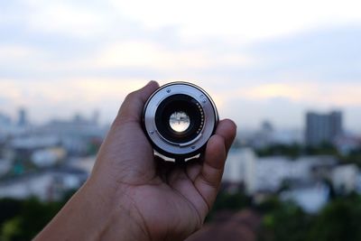 Close-up of hand holding lens against sky