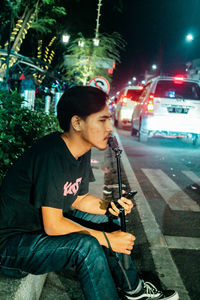 Full length of young man sitting on street at night