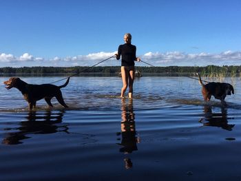 Portrait of young woman with dog standing on lake against sky