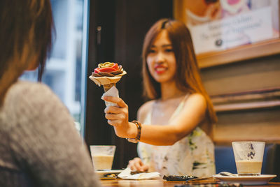 Woman giving ice cream cone to female friend in restaurant
