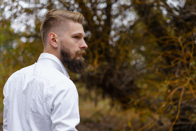 Young bearded man in white shirt walks on yellow autumn day in park. spending