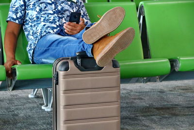 A passenger sitting in a chair, resting while resting his feet on his suitcase