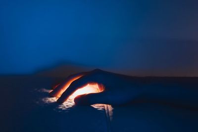 Close-up of hand covering illuminated light on sofa at night