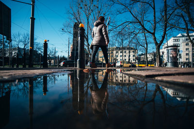 Reflection of bare trees in city against sky