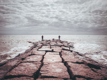 Men fishing by sea against cloudy sky during sunny day