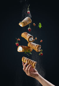 Baked crispy tubes with whipped protein cream levitate on a black background, powdered sugar pours 