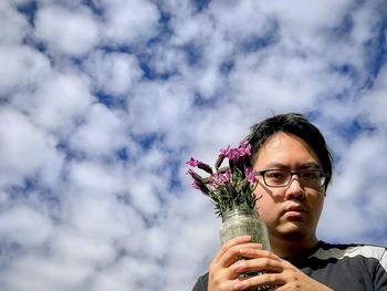 Portrait of man holding flower against sky