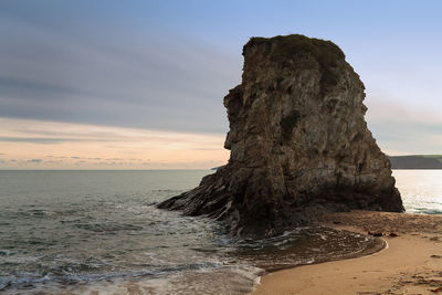 Rock formation on beach against sky during sunset