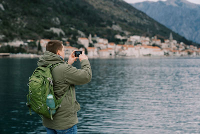 Side view of man photographing sea against mountain