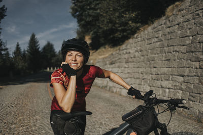 Smiling woman wearing helmet leaning on bicycle seat