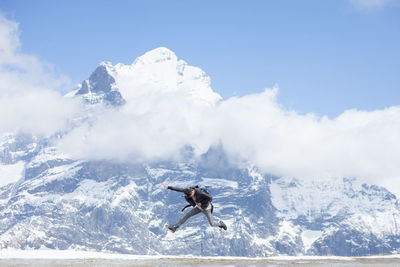 Excited man jumping against snow covered mountain