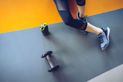 Low section of woman sitting by water bottle and dumbbell on floor