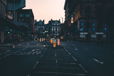 City street by buildings against sky during sunset