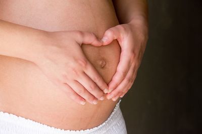 Midsection of pregnant woman making heart shape on belly