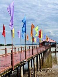 Multi colored flags on pier at beach against sky