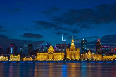 Illuminated buildings by river in city against sky at night