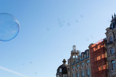 Low angle view of bubbles and buildings against clear blue sky