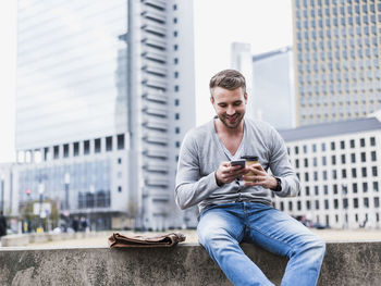 Young man sitting on wall reading text messages