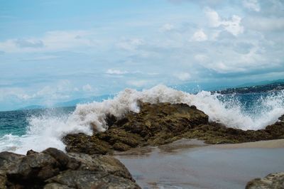 Waves splashing on rocks at shore against sky