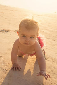 Little baby girl is crawling on a sandy beach near to sea in sunset sunlight.