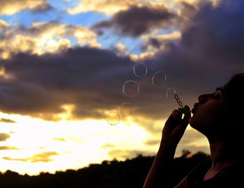Low angle view of silhouette person holding bubbles against sky during sunset