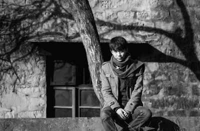 Portrait of young woman sitting against wall