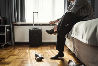 Low section of businesswoman tying shoelace sitting on bed at hotel room