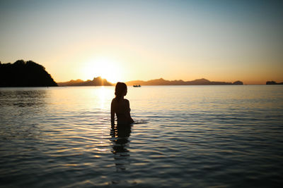 Silhouette woman in sea against sky during sunset