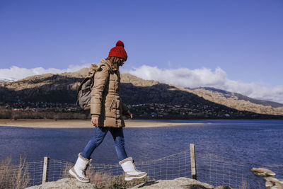 Side view of woman walking on rocks by lake and mountains against sky