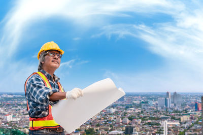 Young man wearing hat while looking at construction site against sky