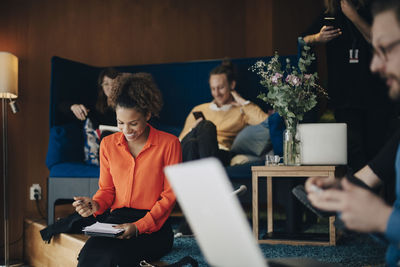 Smiling businesswoman sitting with notepad amidst colleagues at office in cafeteria