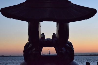 Silhouette statue of liberty seen through navy memorial eagle at battery park during sunset