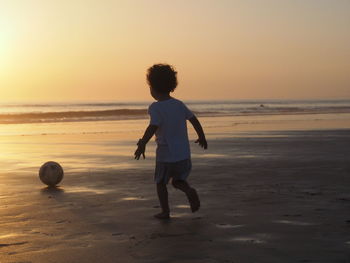 Boy playing with ball on shore during sunset
