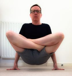 Full length of man practicing yoga against white wall