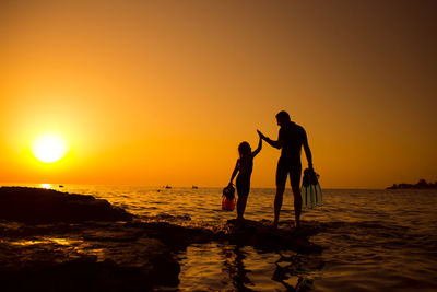 Silhouette people on beach against sky during sunset