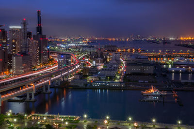 Illuminated city by river against sky at night