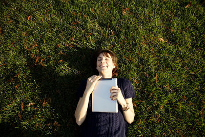 Overhead view of happy woman holding tablet computer while relaxing at park