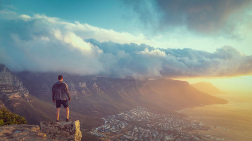 Rear view of man standing on mountain against sky during sunset