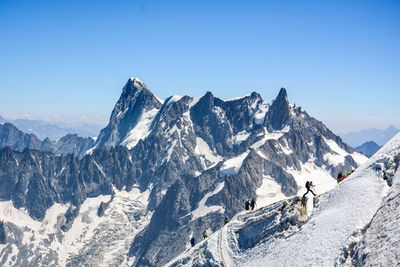 People hiking on snowcapped mountains against clear sky