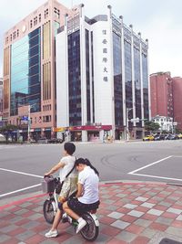 Rear view of people riding bicycle on street against buildings
